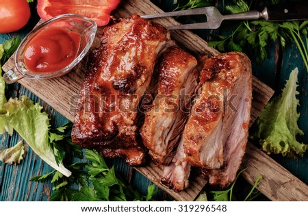 Delicious barbecued ribs seasoned with a spicy basting sauce and served with chopped fresh vegetables on an old rustic wooden chopping board in a country kitchen. Top view.