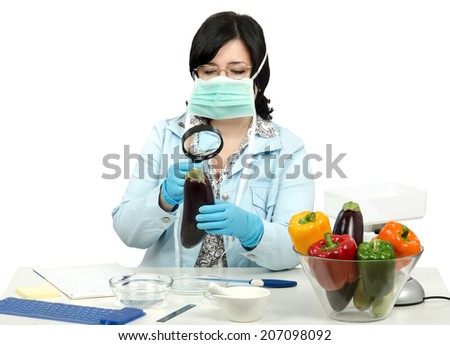 Masked expert carefully inspecting a eggplant with magnifying glass in quality control laboratory