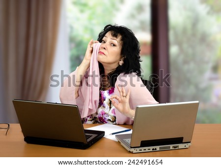 Mature black-haired woman is crying in front of two laptops