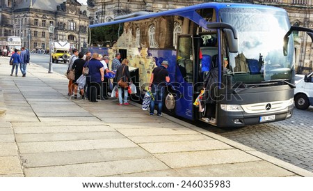 Dresden, Germany - September 30, 2014: Foreign tourist group is leaving Dresden on bus. They holding full shopping bags. Old city palaces reflected in the windows of the big blue coach bus