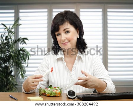 Black haired businesswoman sitting at desk is healthy eating fan. She orders takeaway vegetable salad every lunchtime.