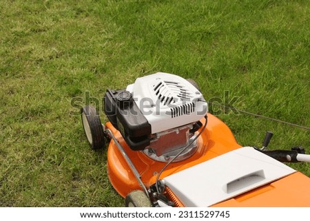 Close up orange-grey electric lawn mower on bright lush green lawn. Gardening work tools. Rotary lawn mower machine cut grass. Professional lawn care service. Place for text. Foto stock © 