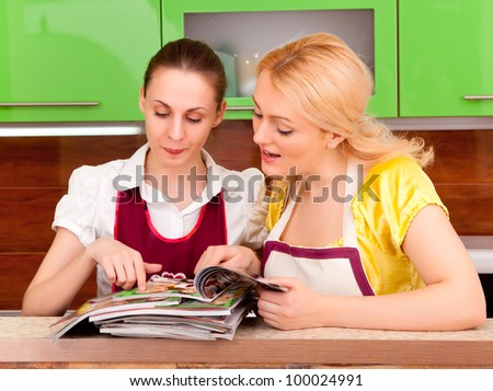 Two young women discuss fashion magazines in the kitchen. Magazine covers are made from the same photo
