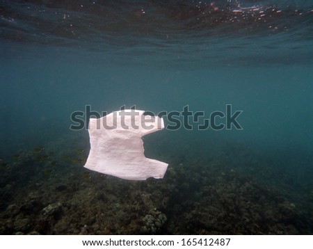 White Plastic Bag floats in the water of the ocean of Hanauma Bay on Oahu, Hawaii.  With Coral and fish in the distant background and sun light shining through the surface.