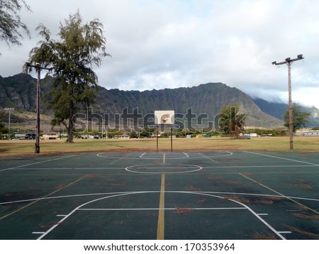 Old rusty Empty Outdoor Basketball Court with lights on wooden poles and pine needles on the court during the day with Mountain range in the background in Waimanalo Beach Park on Oahu, Hawii.