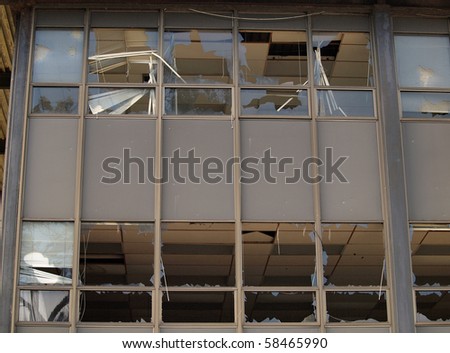 Broken windows of an office building with blinds hanging out the windows.