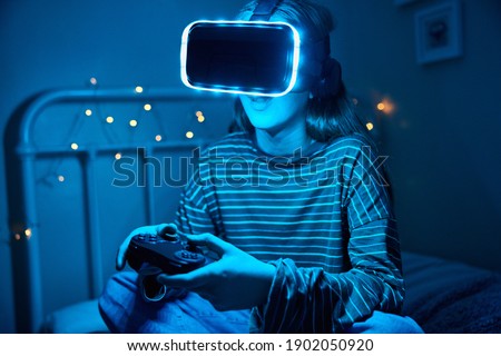 Similar – Image, Stock Photo Teenager girl playing video game at home. Gamer playing online in dark room lit by neon lights. Competition and having fun