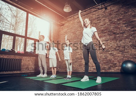 Woman smiling and raising her hands up while doing exercise. Small children repeat the exercise after their parents in the gym.  Foto stock © 