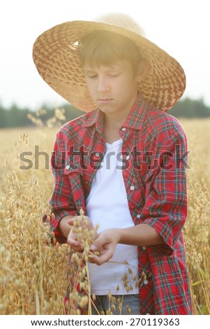 Portrait of teenage farmer boy is holding ripe oat seeds with outer shells in cupped palms with sun flare