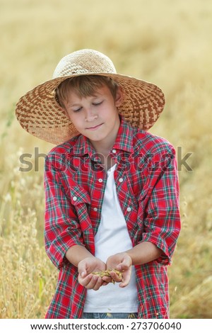 Portrait of teenage farmer boy is checking golden yellow oat seeds in cupped palms at harvest time field