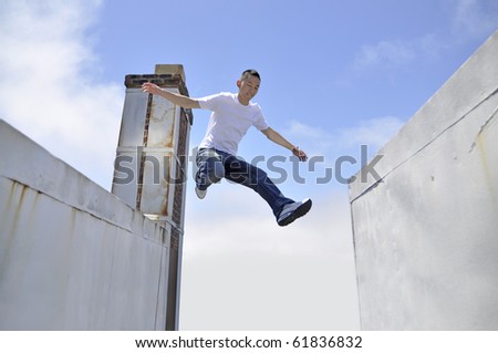 Asian young man making a giant leap in between buildings