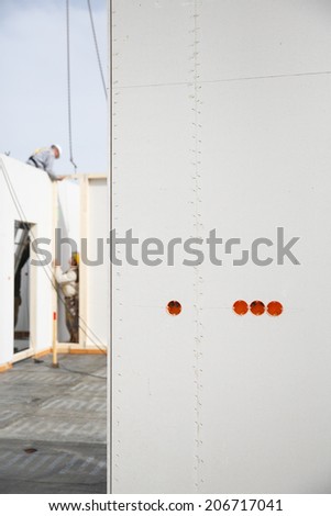 Electricity sockets in a drywall with tubing for wires and workers in the background