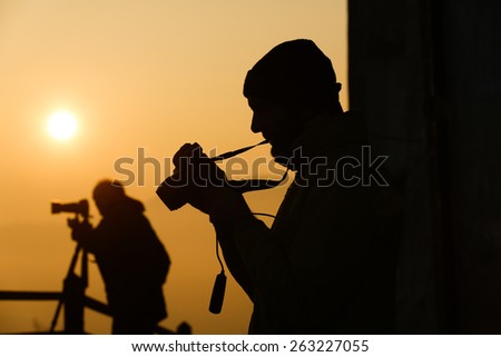 Silhouette of photographers taking photos of an amazing sun at the top of a hill. Amateur and professional working together.