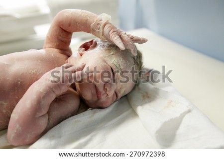 Midwife attending to a newborn baby, covered in vernix after the delivery. Maternity hospital delivery room, baby being photographed for the first time, being measured and assessed for apgar score.