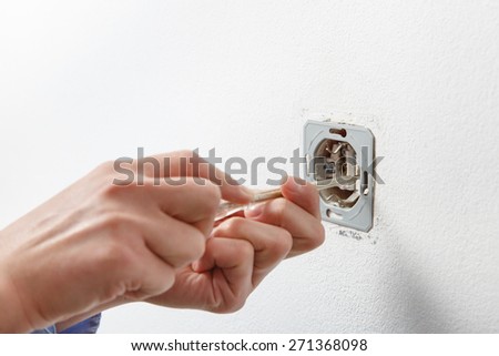 Electrician installing a wall-mounted AC power socket with a screwdriver on a white wall, renovating home.