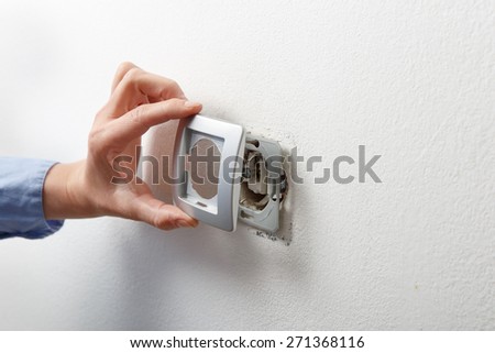 Electrician installing a silver wall-mounted AC power socket with a screwdriver on a white wall, renovating home.