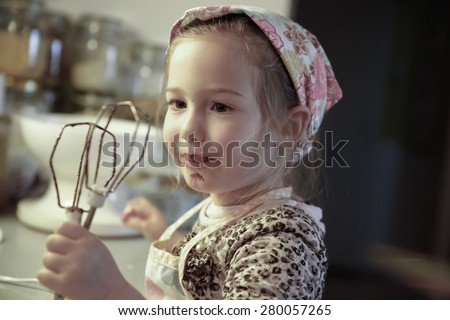 Little girl licking chocolate off the mixer beater after mixing dough for birthday cake. Permissive parenting, learning through experience, child inclusion, homemade food concept.