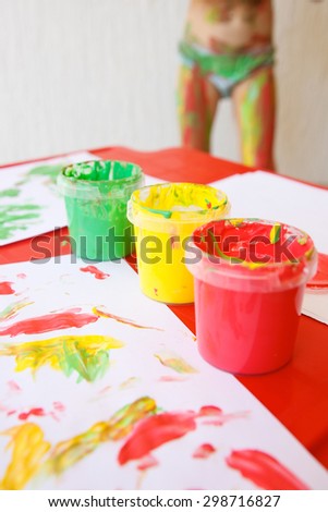 Finger paints in bright colors, used for finger drawings and sensory play, with drawings and body painted girl in the background. Innovative approach to learning, fun childhood concept.
