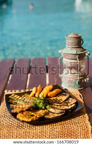 Serving of grilled zucchini, chicken and eggplant blue/Plate of plenty grilled food on picnic table. Lantern on serving table with serving plate. Grilled vegetable.