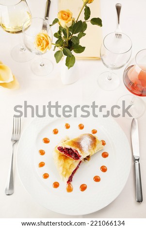 Cherry pie served on white plate in elegant fancy restaurant. Served table with decorative flowers/Traditional cherry pie