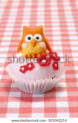 Chocolate cupcake covered with pink fondant. Cupcake on picnic table./Chocolate cupcake with owl