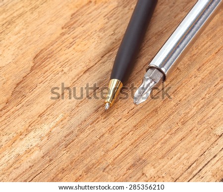 Pen and a screwdriver on the old wooden floor.