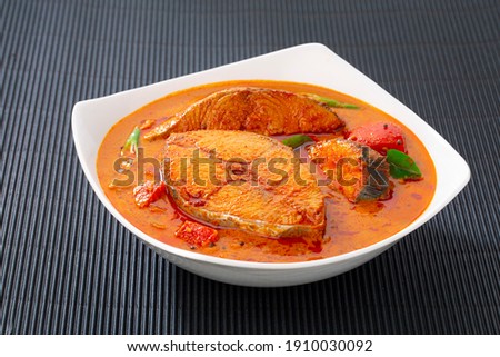 Fish curry_Seer fish curry ,traditional Indian fish curry ,kerala special dish using coconut ,arranged in a white bowl garnished with curry leaves  on black textured  background, isolated.