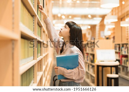 Female college student looking for a book in the library