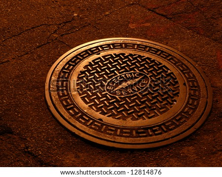 And electric service manhole cover shinning in soft copper tone under the street lights at night