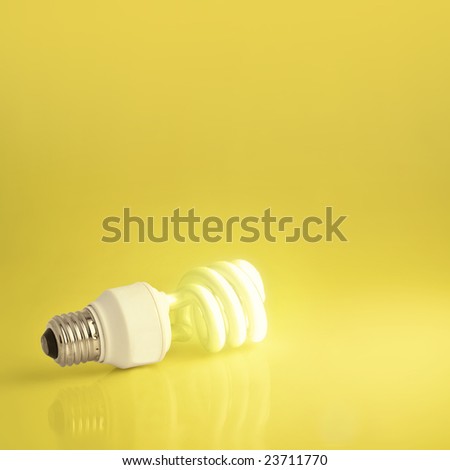 A vibrant presentation of a modern green energy-saving lightbulb lit on a golden background.  Plenty of copyspace