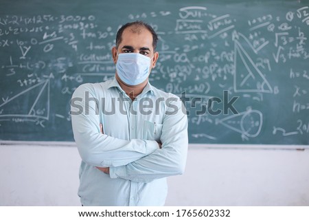 Portrait of male teacher wearing mask standing against blackboard teaching mathematics in classroom, school reopen after lockdown due to covid-19 pandemic. new strain of coronavirus, omicron cases 