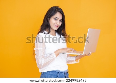 Portrait of happy young indian girl wearing white T-shirt using laptop isolated over orange yellow background. Studio Shot, Copy space, Asian woman using computer. Technology concept. Foto stock © 