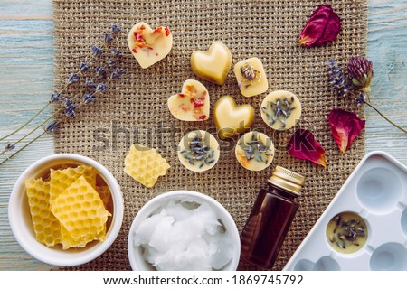 Making of mini wax melts for aroma lamp diffuser at home concept. Tools ingredients on table unbleached beeswax, solid coconut oil, essential oil, dried flowers and plastic mold. Flat lay view.