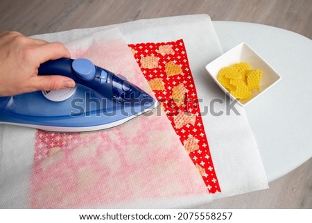 Close up view of person woman make beeswax  wraps for wrapping food in home indoors, alternative for plastic. Use iron machine to melt beeswax into cotton cloth.