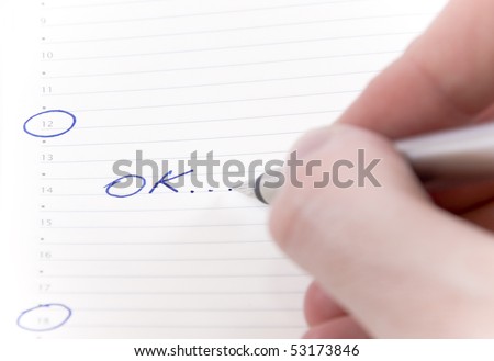 Man hand writing OK with a pen on a calendar paper,