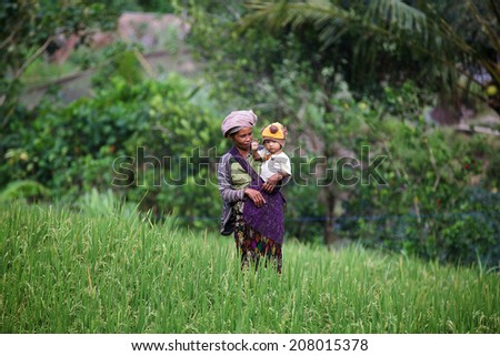 BALI, INDONESIA - JULY 9: Balinese woman with unidentified child welcomes tourists in Ubud rice field, Bali on July 9, 2014
