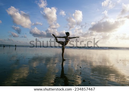 Young woman practicing warrior pose from yoga on the beach at sunset