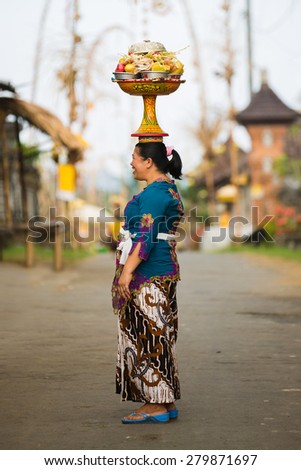 BALI, INDONESIA - JUNE 2: Balinese woman loads the offering of food in wooden jar on her head for the ceremony in Ubud temple, Bali on June 2, 2014