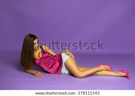 Fashion Studio Photo of Glamor Stylish Beautiful Young Woman Model in Summer Bright Colorful Cloth. Fashionable Look, Tan, Long Healthy Hair. Girl Lying on the Floor at Studio
