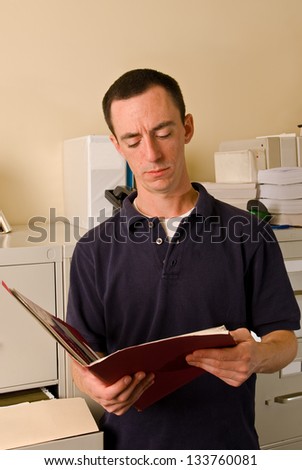 Caucasian male in file room reading papers inside a folder