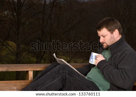 Man drinking coffee and reading a newspaper outside on a cool fall morning