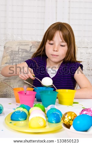 Young girl in the process of coloring Easter Eggs - Step two, the egg on a spoon about to be lowered into the cup of dye