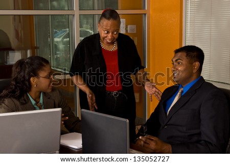 Two young business professionals smile as their more mature, wiser officer manager explains to them how things should be done.