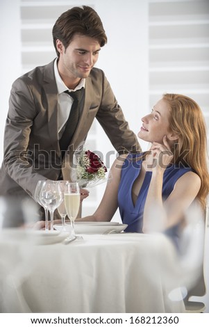 romantic man giving flowers to his girlfriend in a restaurant