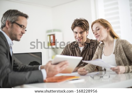 real-estate agent shows a build project on a digital tablet to a young couple