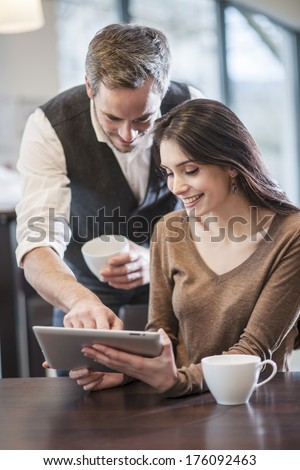 two young people around a digital tablet in a cafe