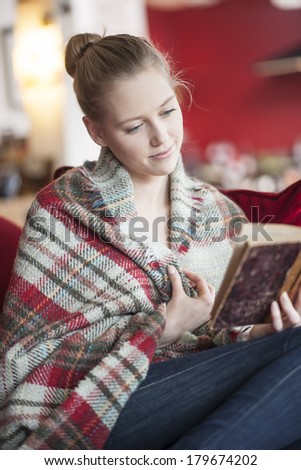 young woman reading a book on a couch a cover on the shoulders