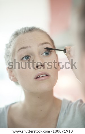 beautiful young woman applying makeup on her eyelashes in front of her mirror