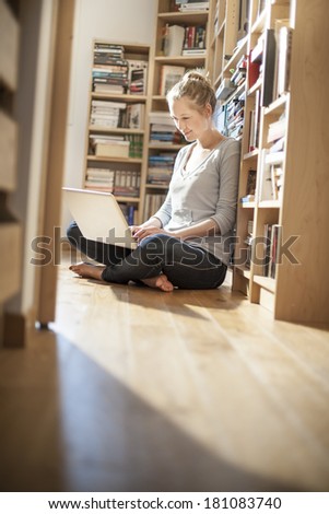 young student sit on the floor working on her computer near family library