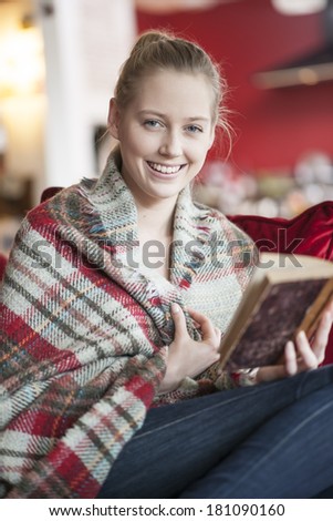 young woman reading a book on a couch a cover on the shoulders
